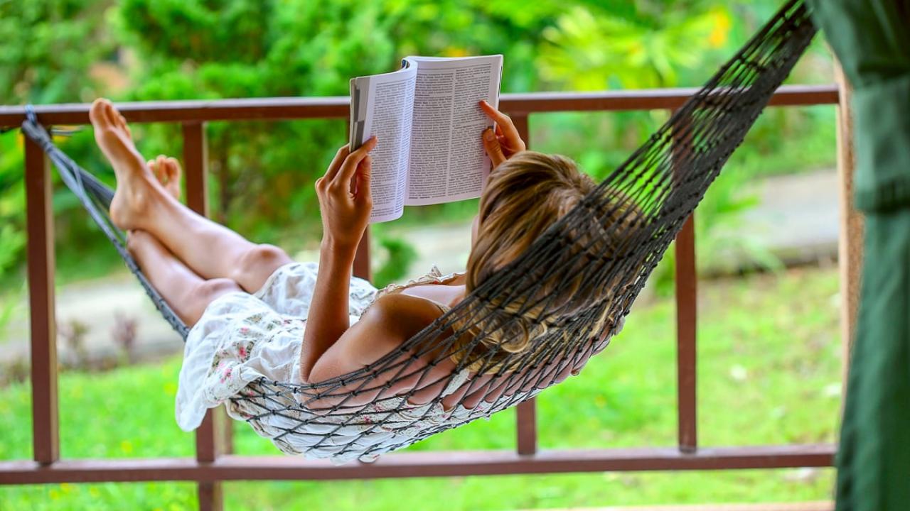 person in white dress reading on front porch, laying in hammock. 