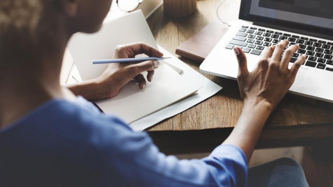 Person sitting in front of laptop taking notes on a piece of paper.