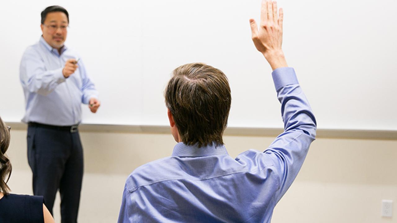 man holding up his hand to ask a question of an instructor