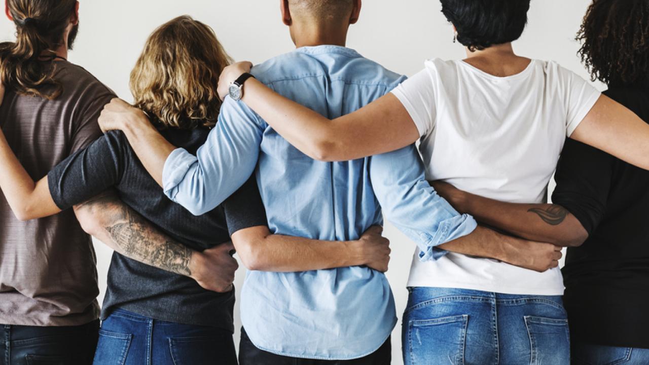 people with backs to the camera, standing in a row, arms around each others' shoulders.