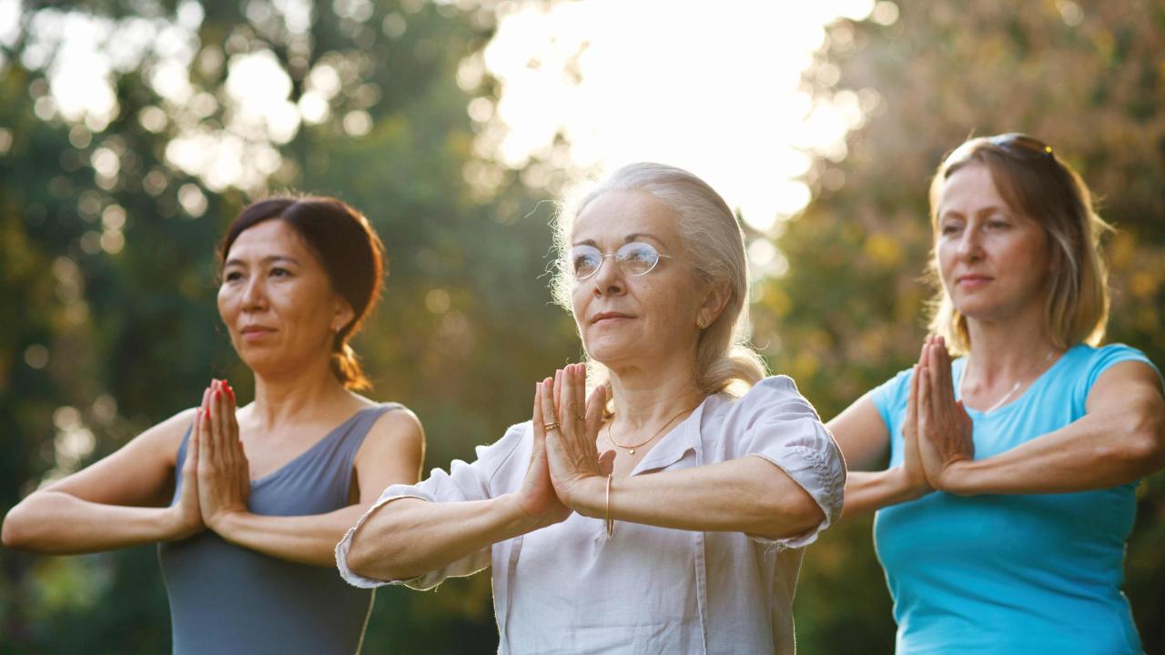 Three women are doing a yoga pose outdoors.
