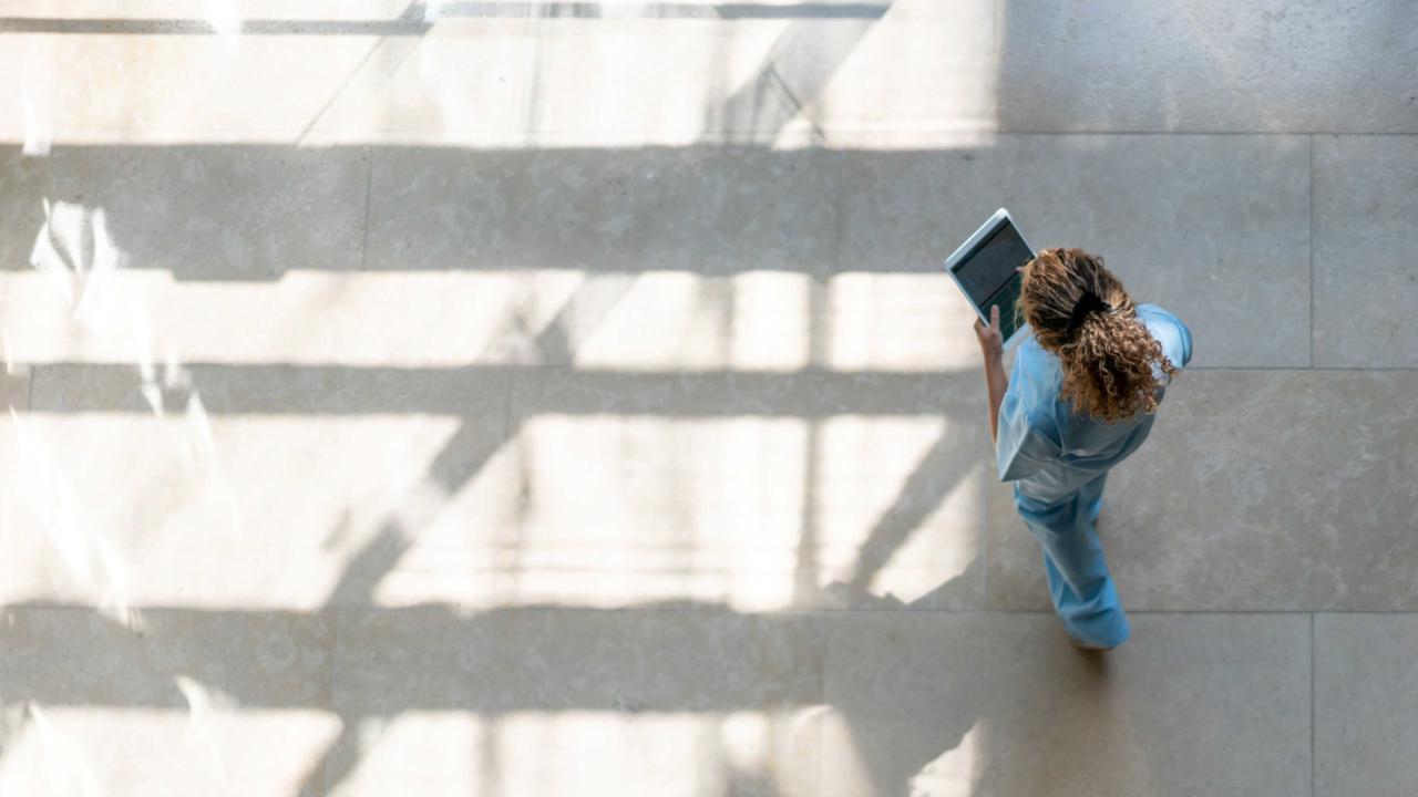 Woman is walking holding a tablet, looking down.  