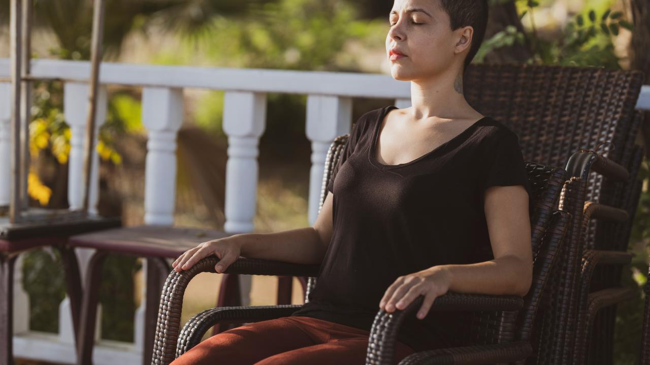 A woman with short hair sits peacefully in a chair, eyes closed, enjoying the sunlight.