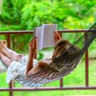 person in white dress reading on front porch, laying in hammock. 