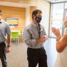 A man and woman are talking to one another and another man is standing directly behind him.  