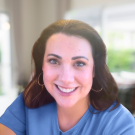Smiling woman in blue top with hoop earrings, indoor portrait photo, blurred background