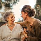 An older woman and younger woman sit outside and smile at each other while holding hands.